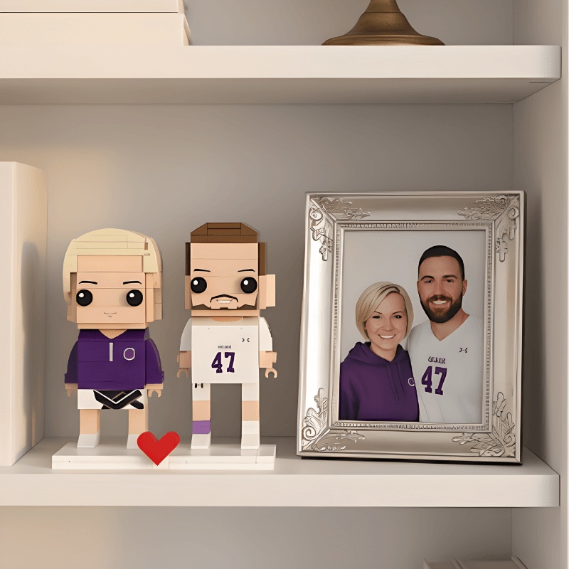 Two personalized mini figurines in front of a framed photograph on a shelf.
