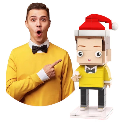 Man in yellow sweater pointing at a LEGO figure with a Santa hat on a pink background