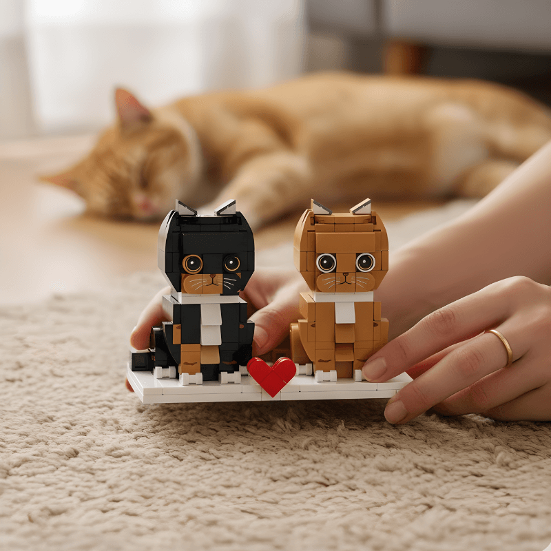 Two brick-built cat figures with a heart held by hands on a carpeted floor with a cat in the background.