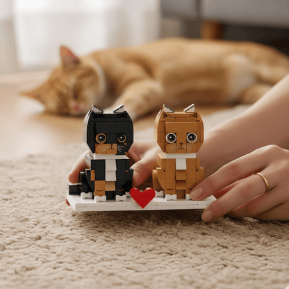 Two brick-built cat figures with a heart held by hands on a carpeted floor with a cat in the background.
