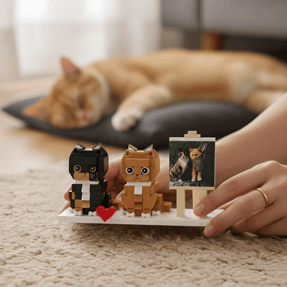 Two cat-shaped toys on a tray with a heart and a small painting, with a cat lying in the background.
