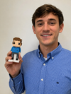 Man holding a small figurine of himself against a plain background