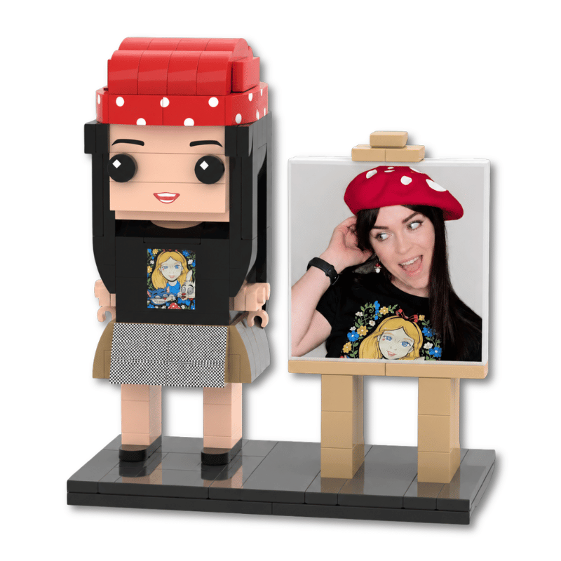 A custom lego minifigure of a woman with a red polka-dot beret, black top, and gray skirt, standing beside a small easel that displays a photo of the same woman wearing the beret and black graphic top. The entire set is built from interlocking toy bricks on a plain white background.