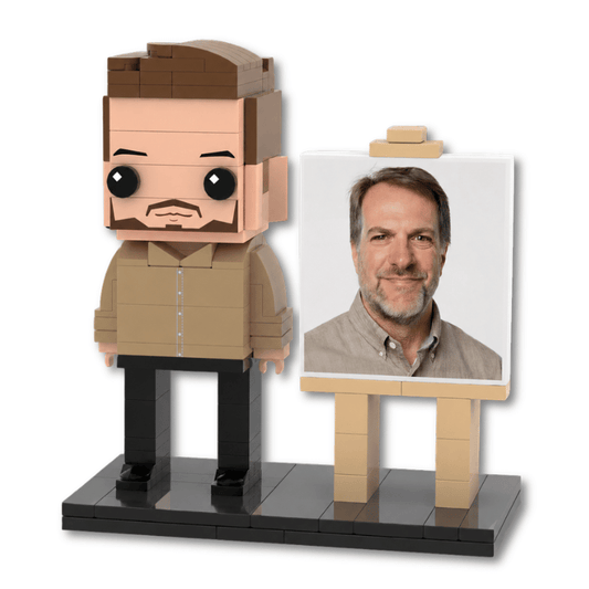 A custom lego minifigure of a man with a beard and brown hair, standing next to a small easel holding a printed portrait of a real man. The figure is wearing a tan shirt and black pants on a black base, set against a plain white background.