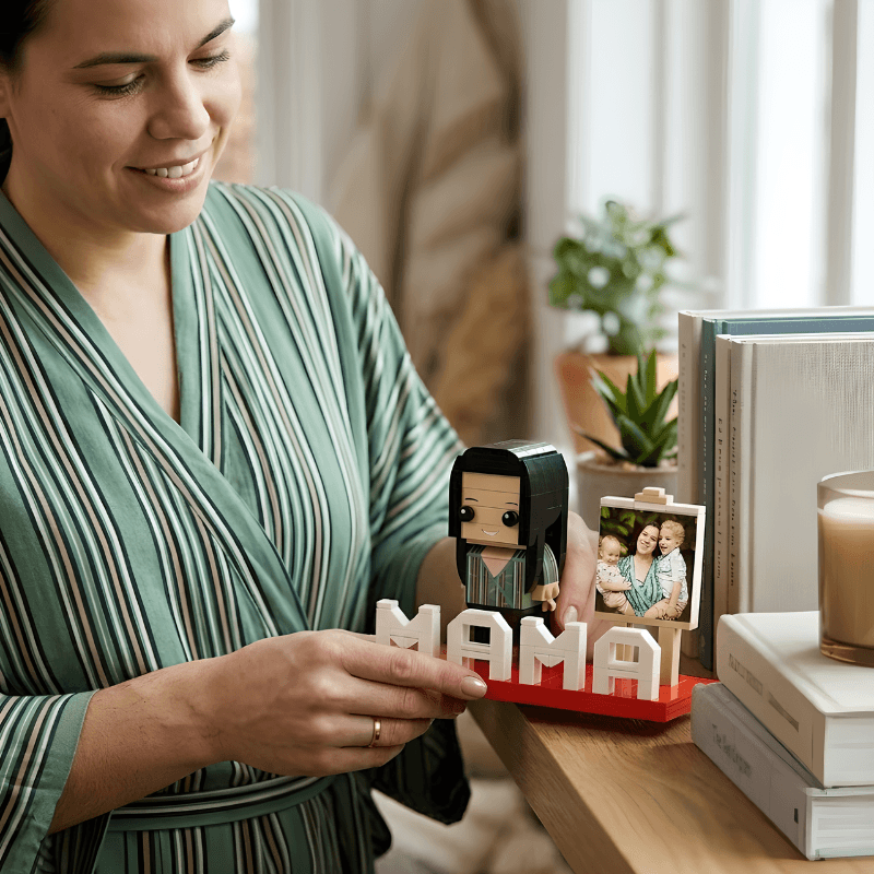 Woman holding a small figurine with 'MAMA' letters and a photo frame in a home setting.
