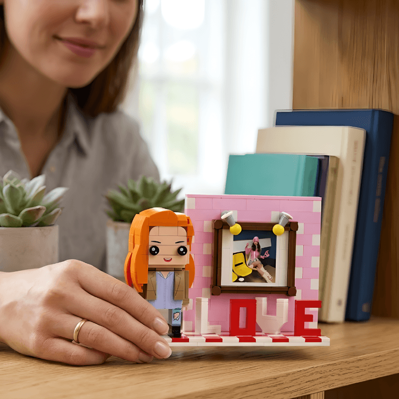 Person holding a LEGO figure next to a LEGO photo frame on a wooden surface.