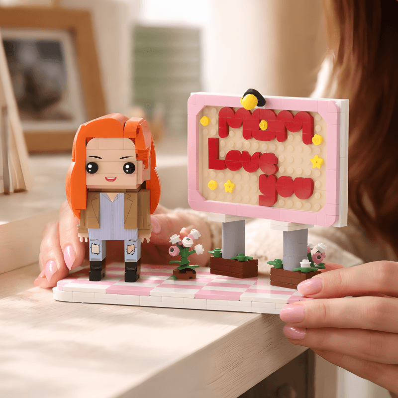 Toy figure of a person with orange hair and a sign saying 'Mom Love You' held by hands.